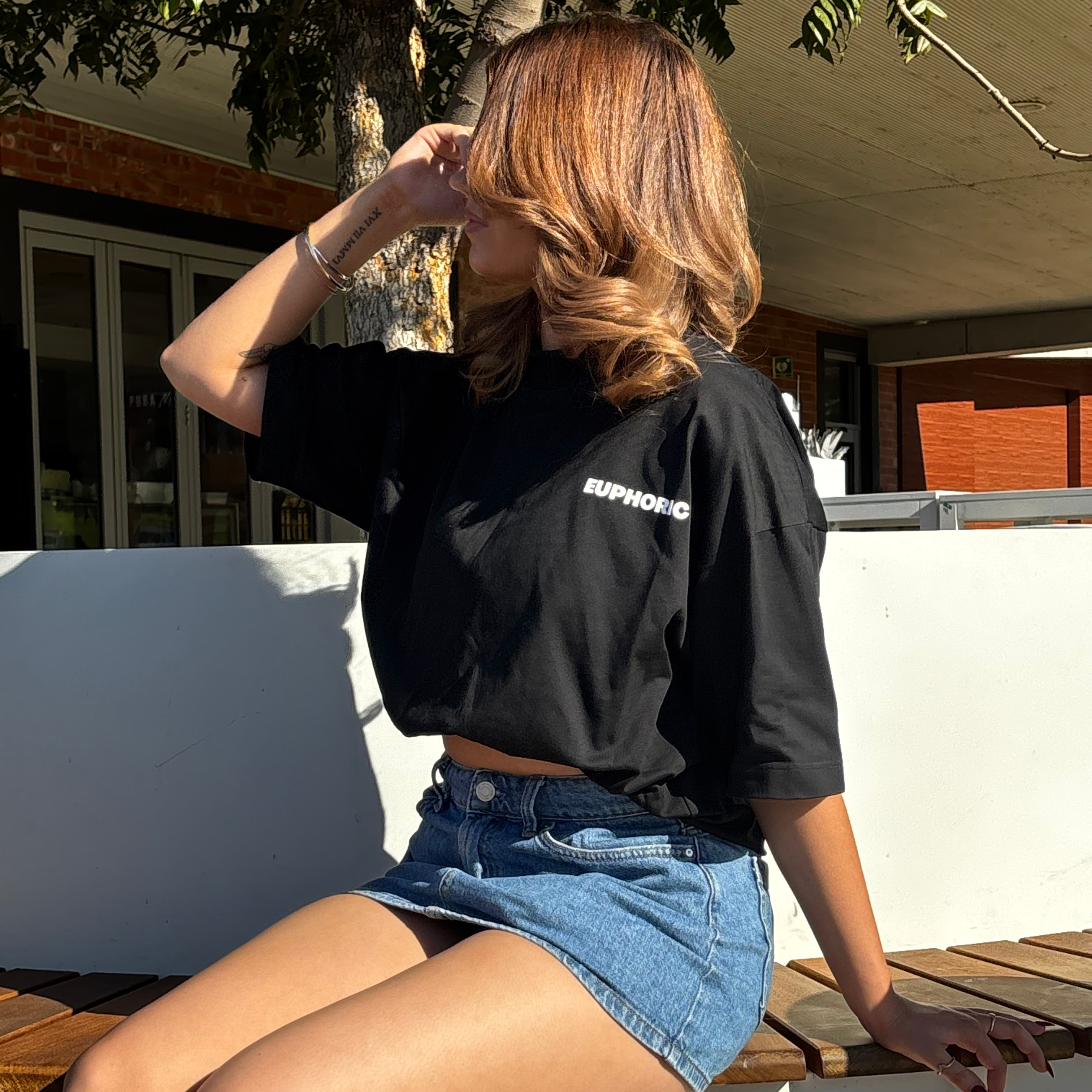 Person wearing a euphoric black t-shirt sitting outdoors.