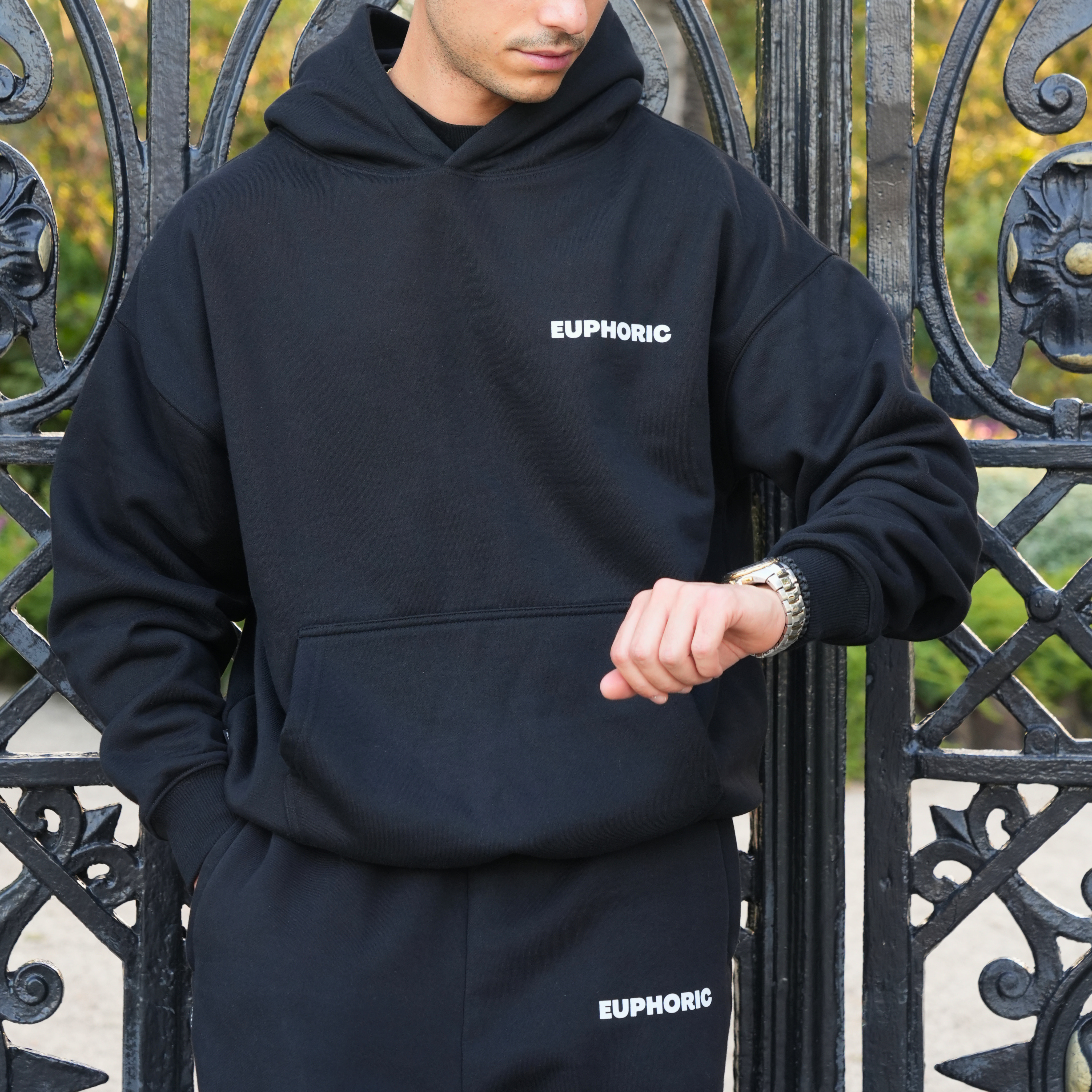 Person wearing a euphoric black hoodie with 'Euphoric' front logo, standing in front of an ornate gate.