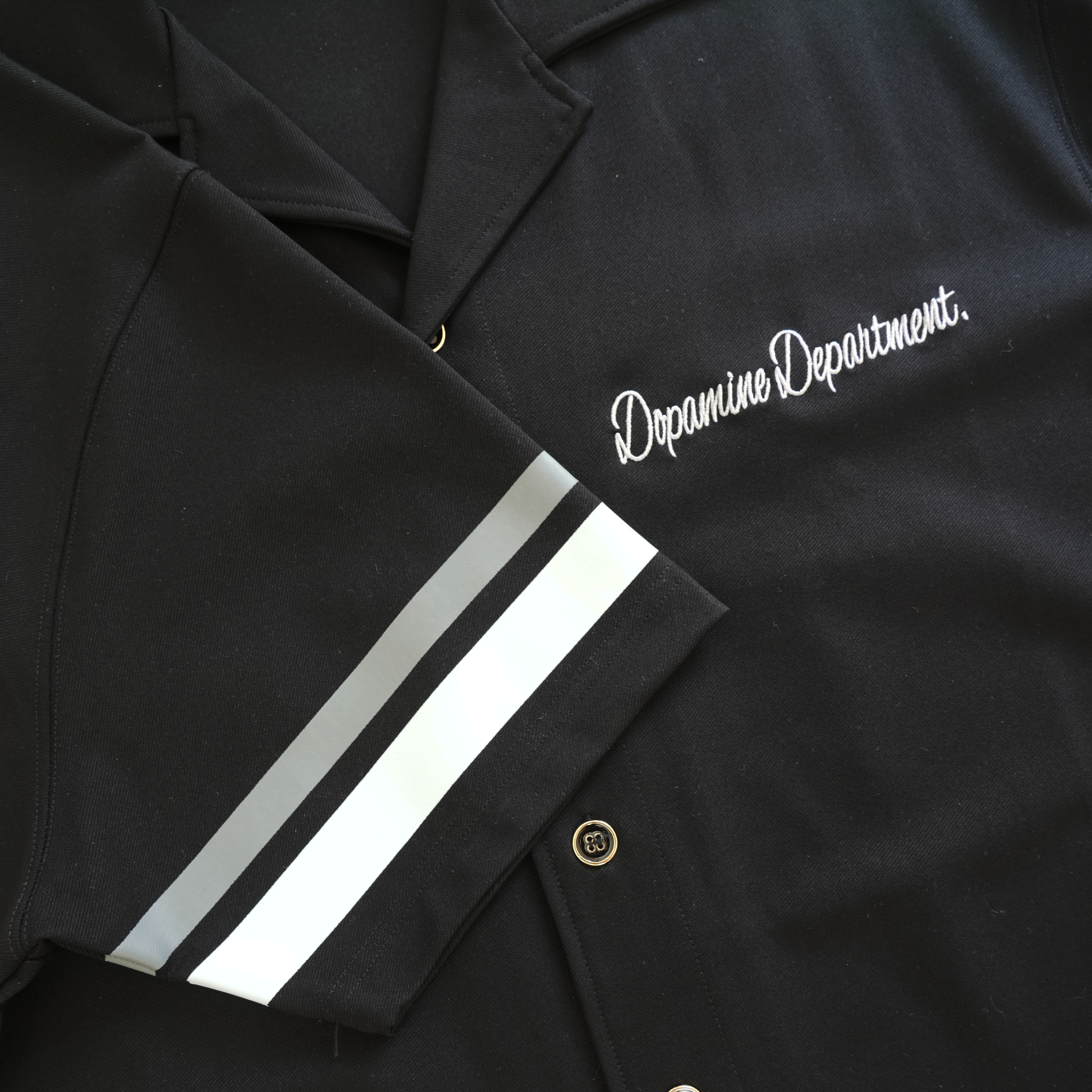 close-up of the front logo, buttons and grey stripes on the sleeve of the euphoric jet black button shirt