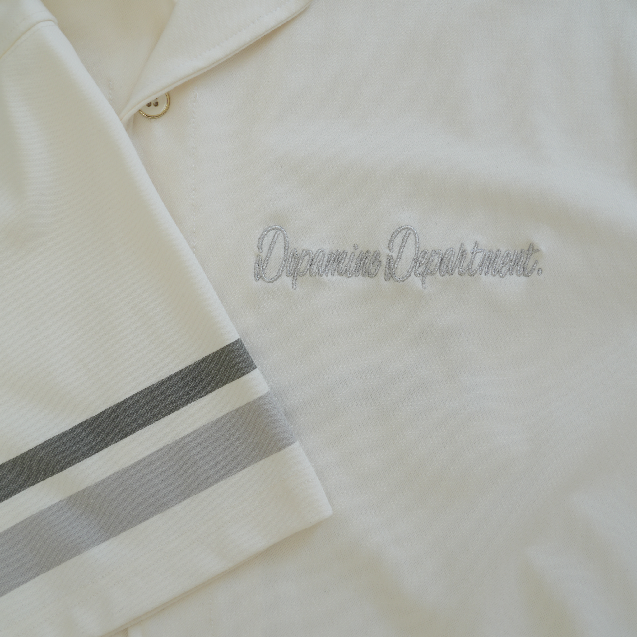 Close-up of euphoric pearl white button shirt, showing the embroidered front logo and grey stripes on the sleeves