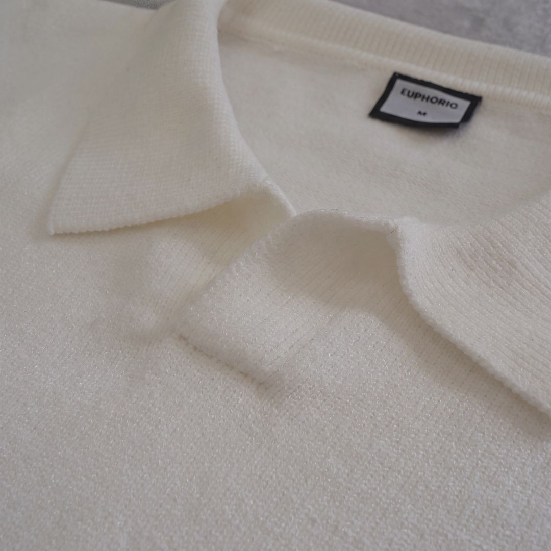 Euphoric pearl white polo shirt collar fold and brand label detail on concrete floor