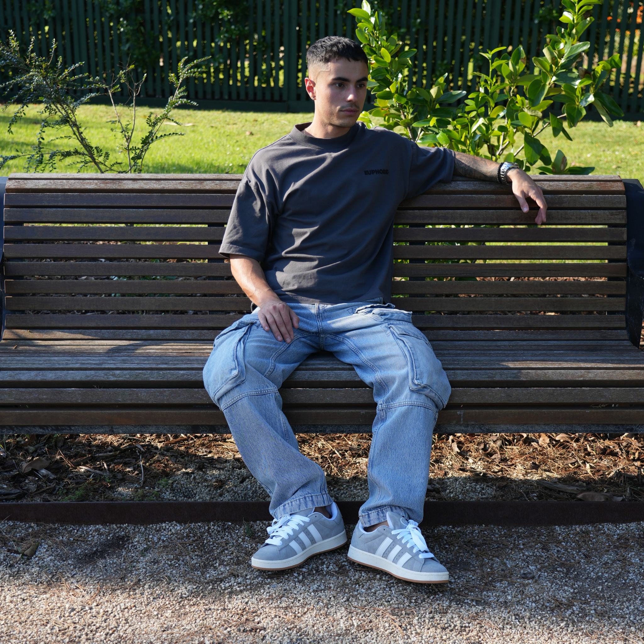 Man sitting on a wooden bench in an outdoor setting wearing a euphoric poppy seed t-shirt