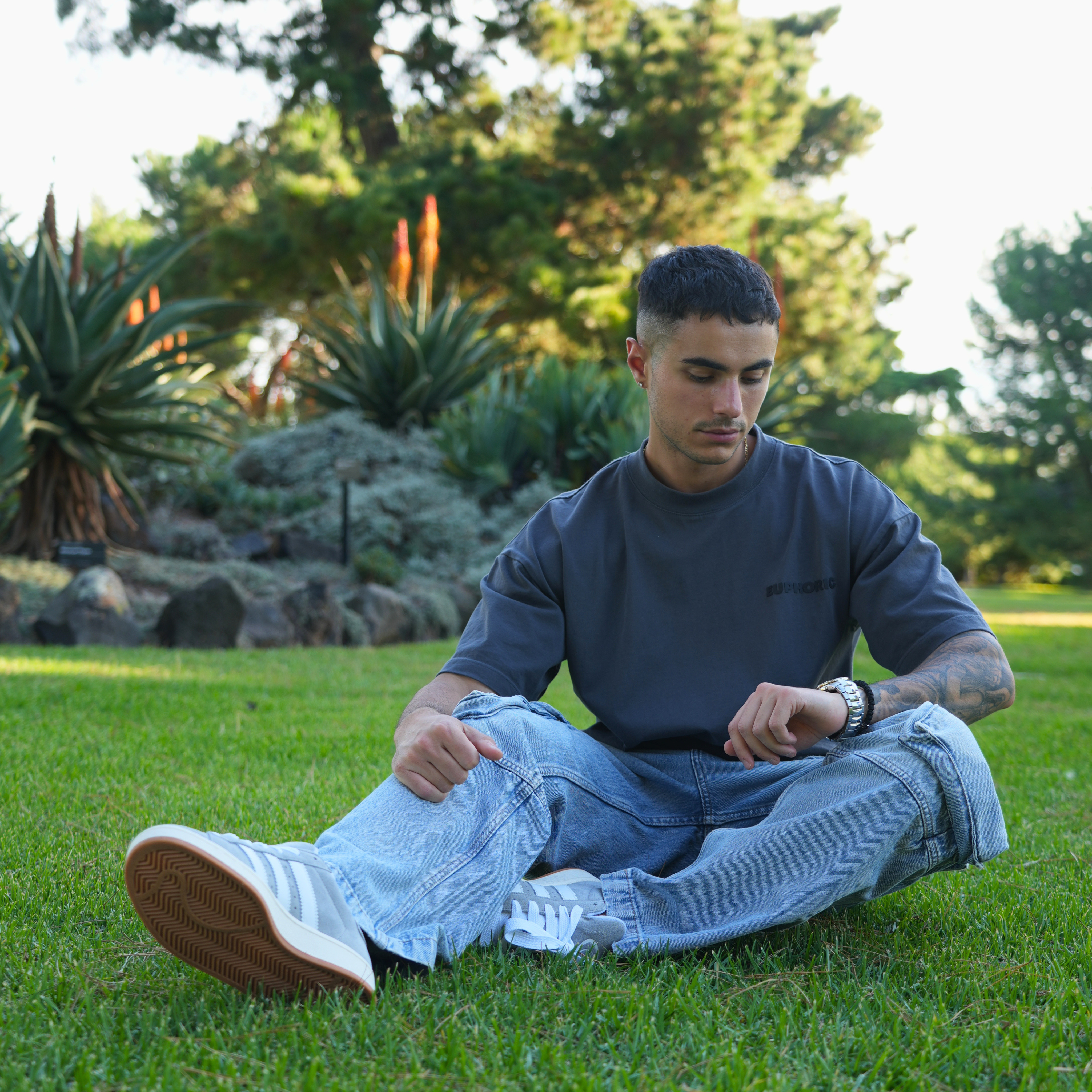 Man sitting on grass in a park wearing a euphoric poppy seed t-shirt with light blue jeans.