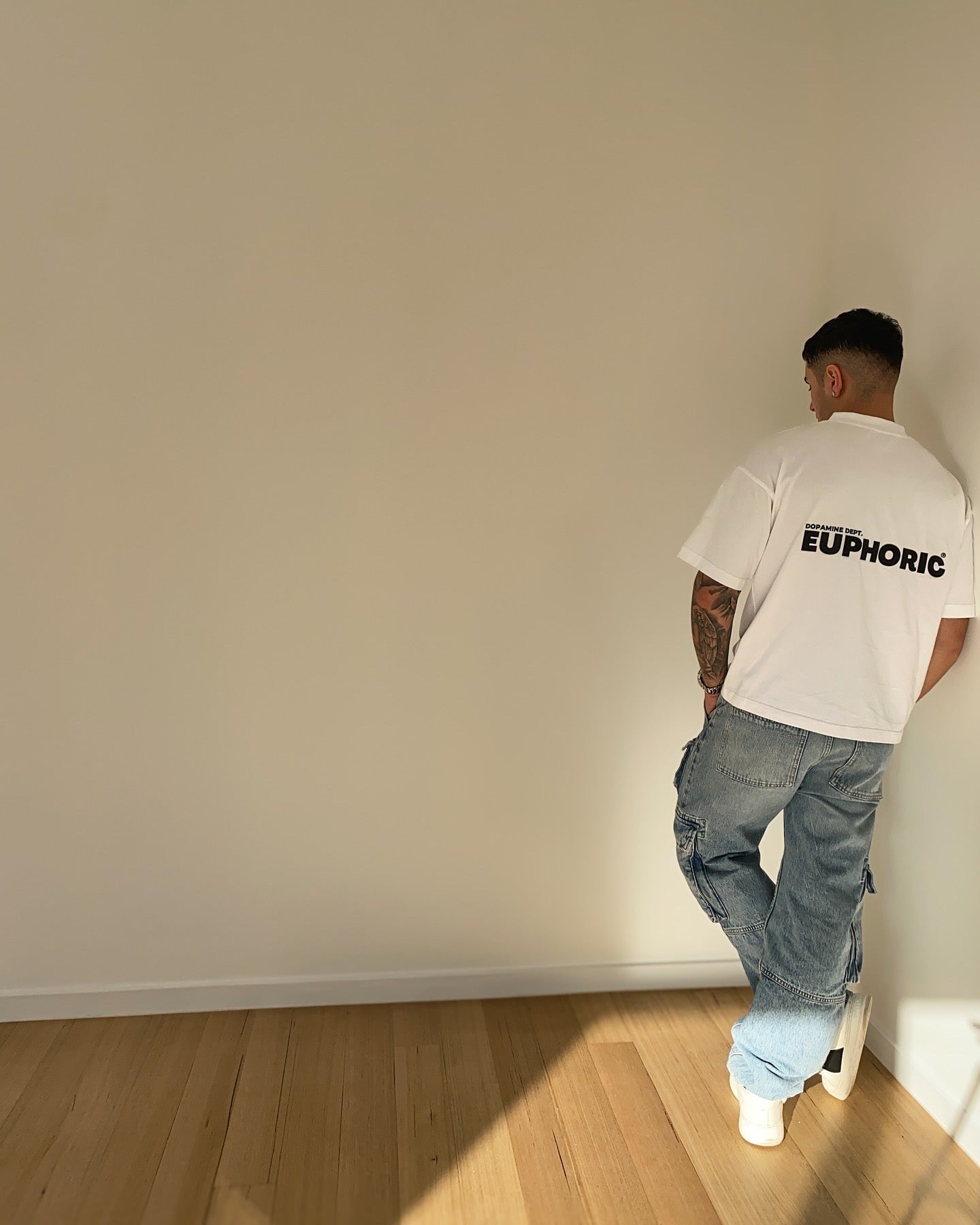 Person wearing a euphoric white t-shirt, standing against a plain wall.
