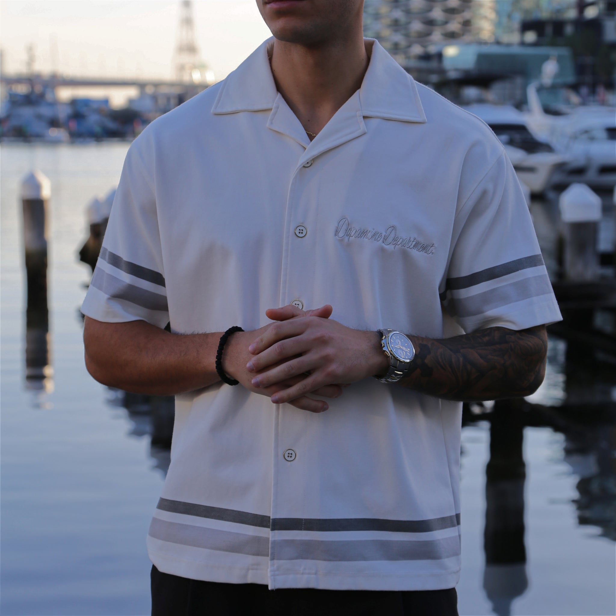 Close up of man wearing euphoric relaxed white button shirt standing by a waterfront with boats in the background