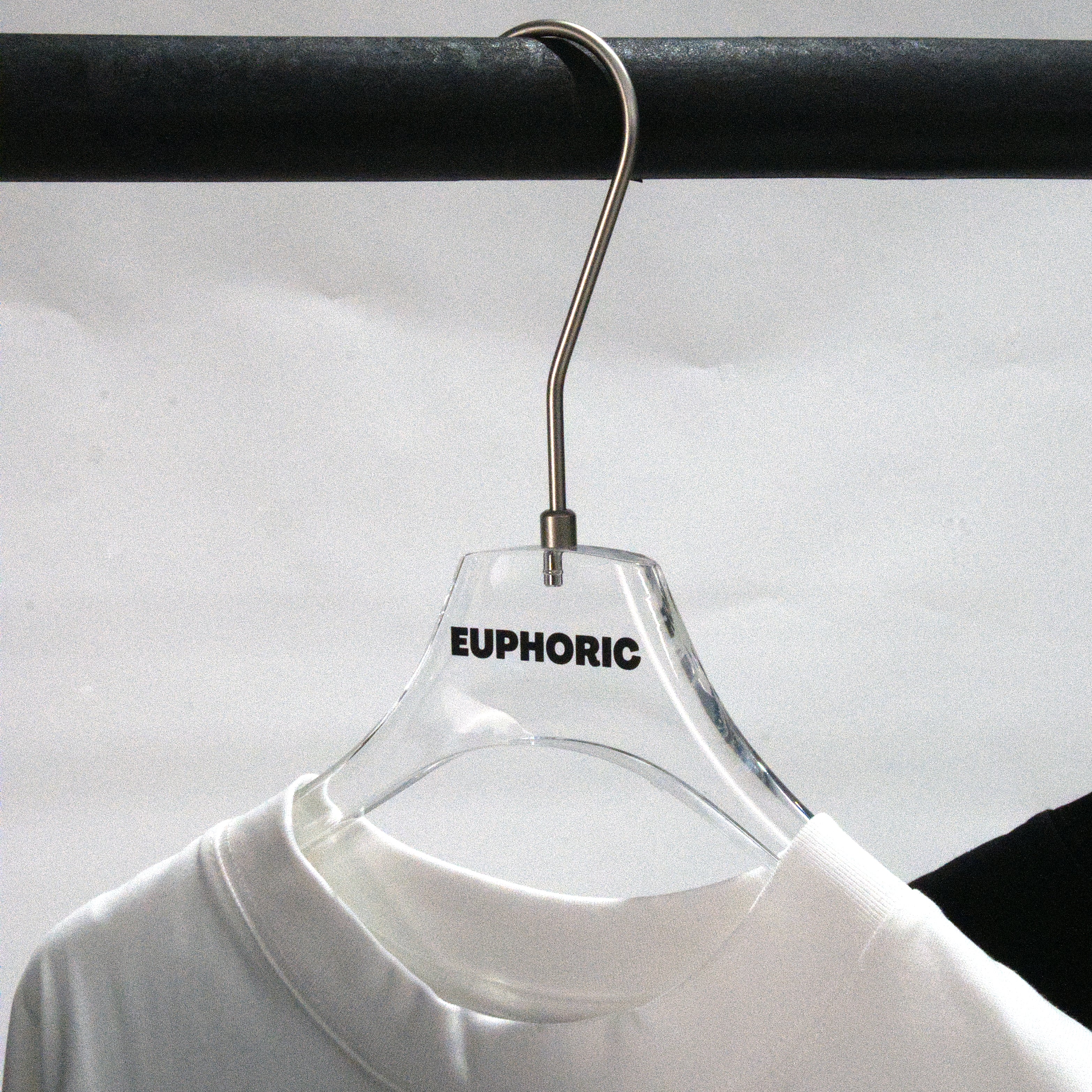 A clear plastic hanger with the brand name 'EUPHORIC' printed in black on the front, holding a white crew-neck t-shirt. The hanger is suspended from a black clothing rack against a light gray background.
