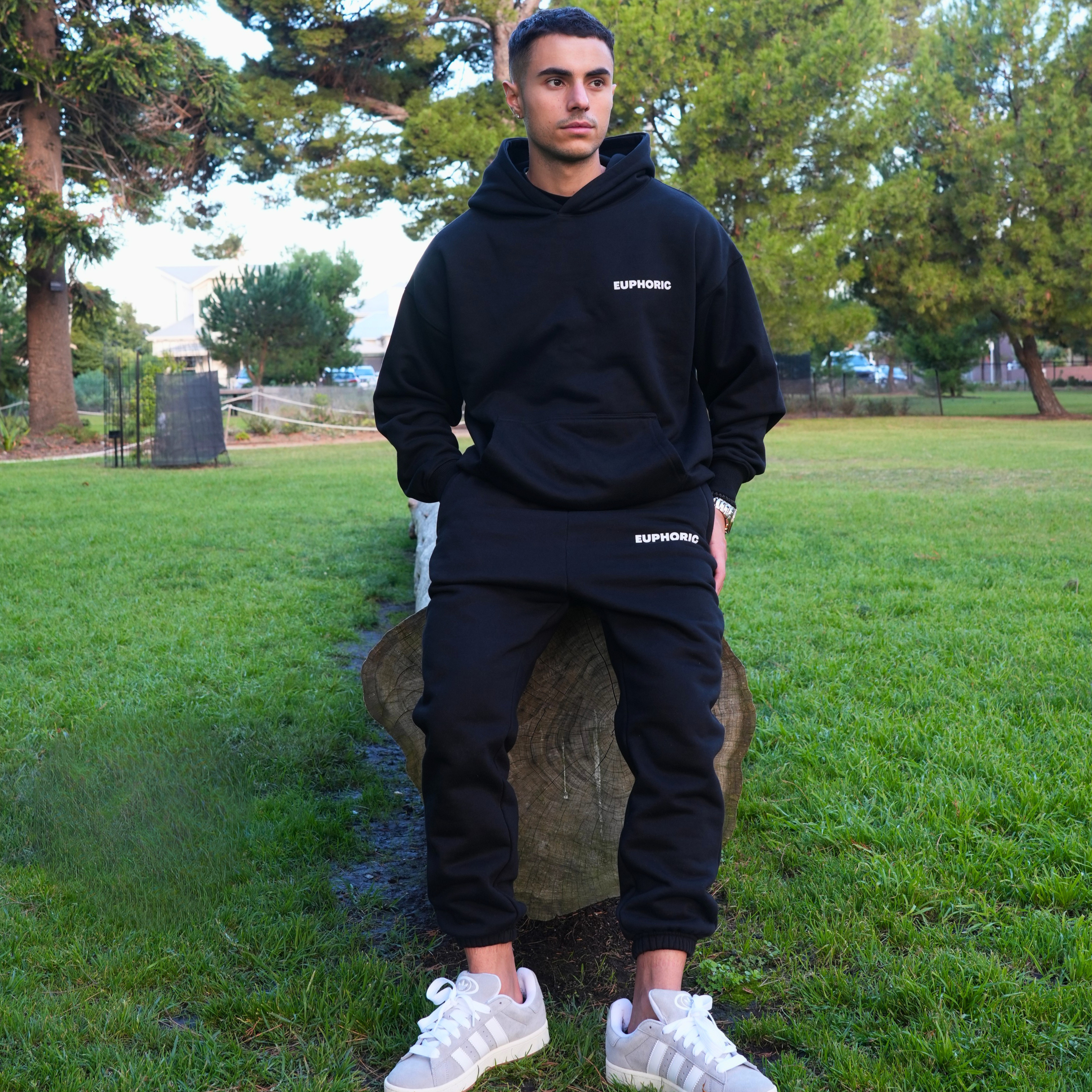 Person wearing a euphoric black hoodie and pants, standing outdoors.
