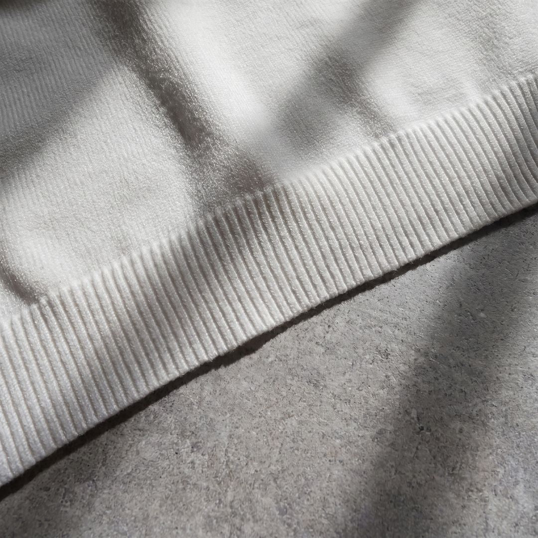Close-up of ribbed hem texture on Euphoric pearl white polo shirt with concrete background