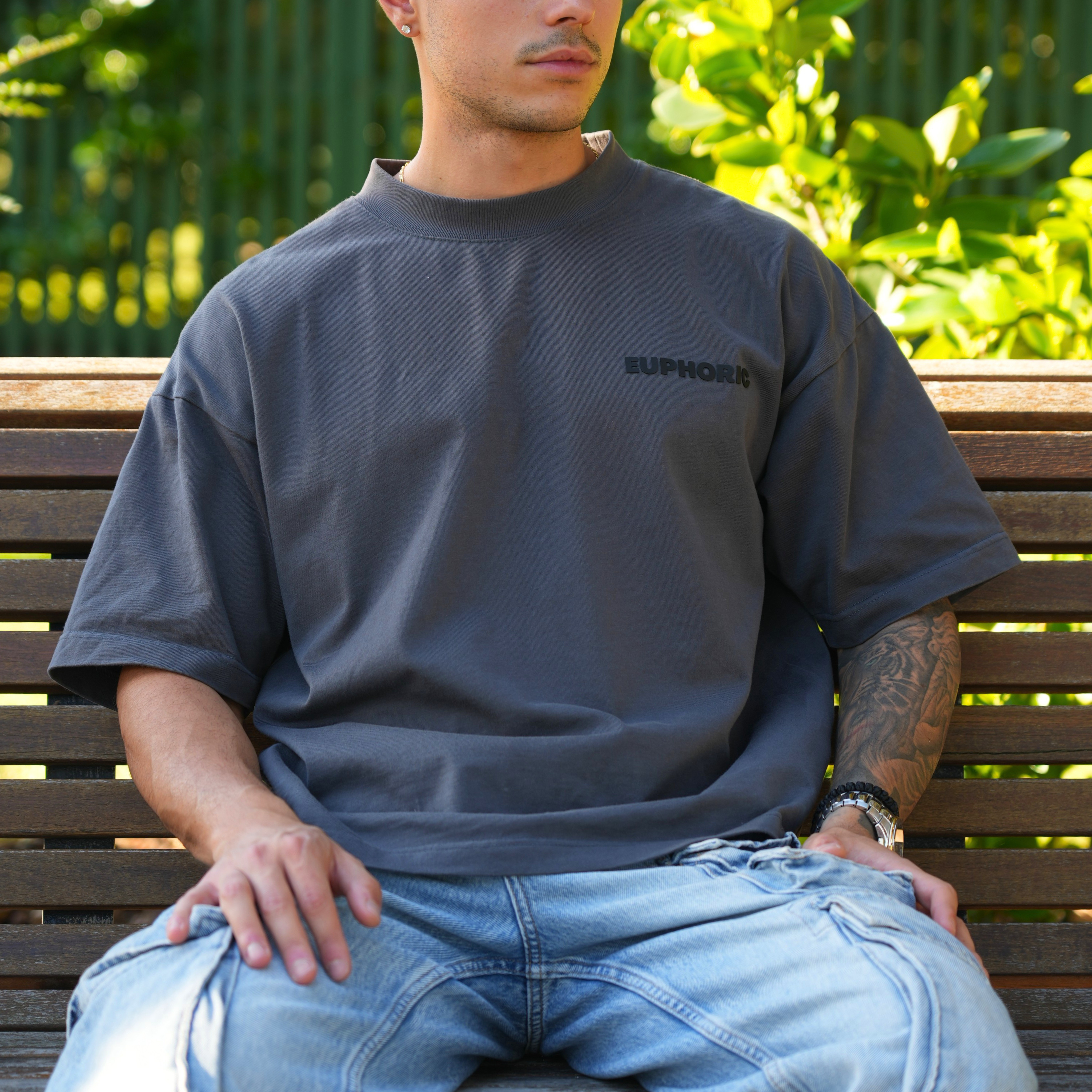 close-up of man wearing a euphoric poppy seed t-shirt, sitting on a wooden bench outdoors.