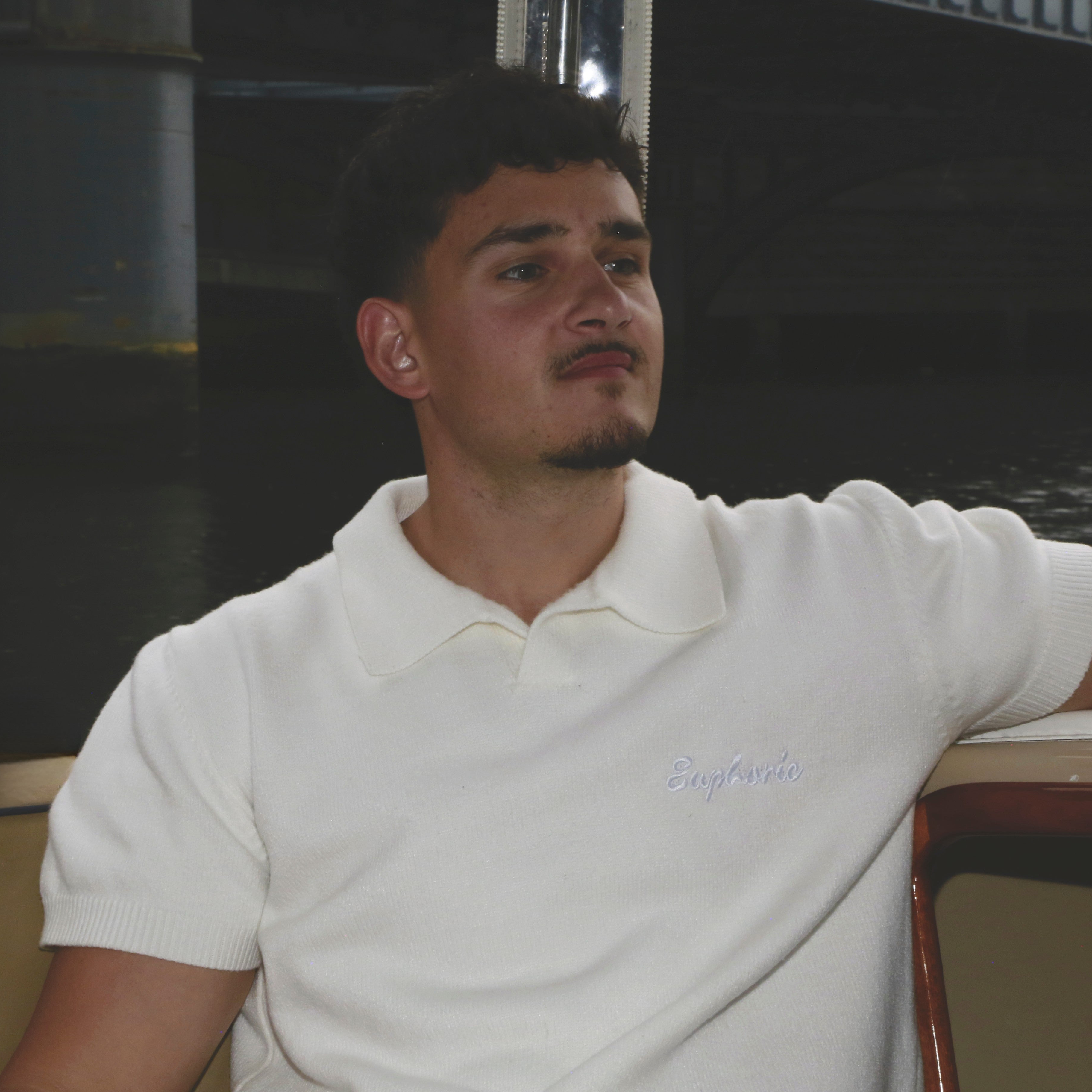Man wearing a euphoric white polo shirt with a logo, sitting indoors.