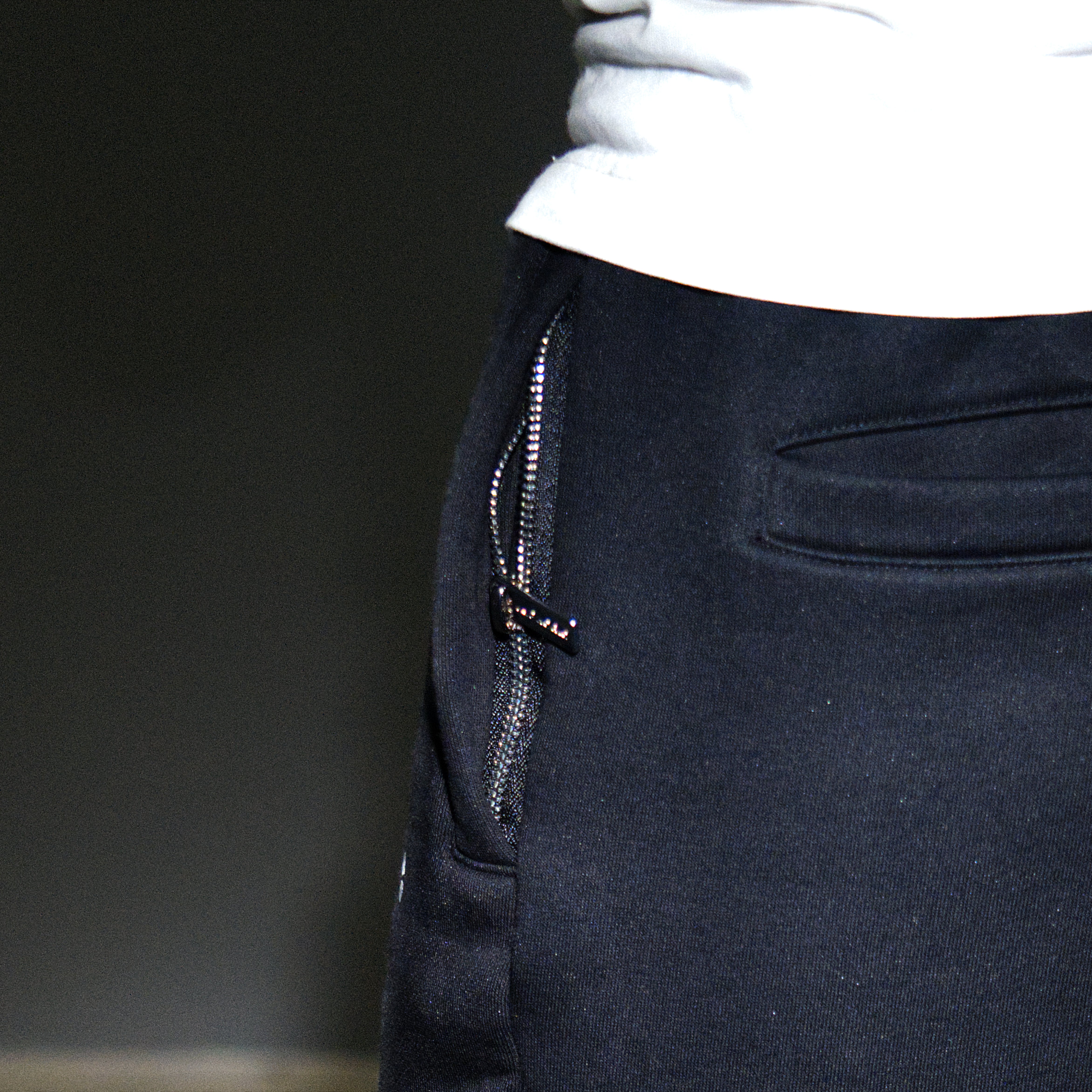 Close-up of a person wearing black euphoric sweatpants with a side zipper and a white top, photographed against a dark background.