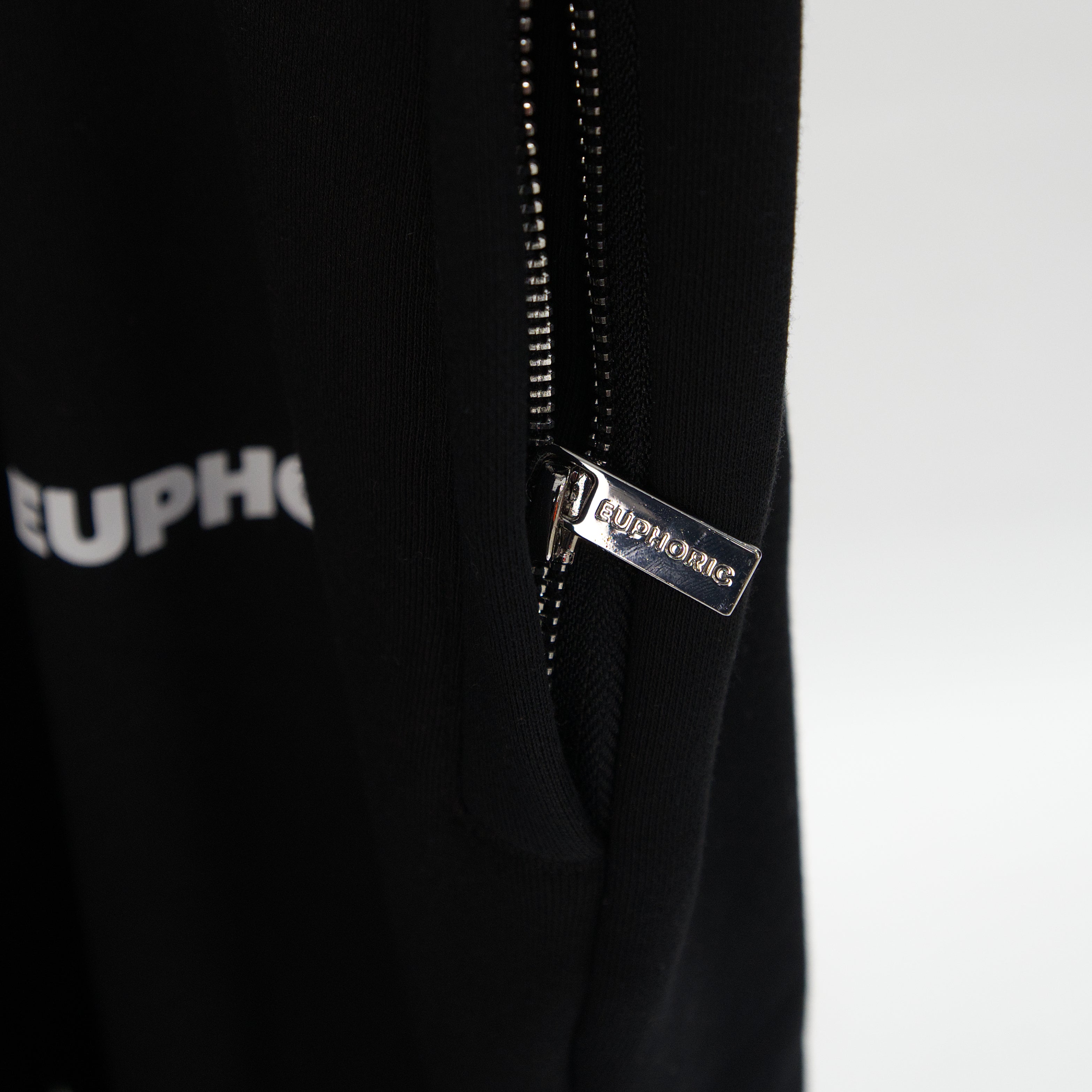 Close-up of a black zippered garment with a silver-tone metal zipper pull featuring the brand name 'EUPHORIC' debossed.